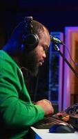 Vertical Music technician with headset mixing and mastering his audio recordings, operating on console in home studio. Musician producer creating new tunes with sound effects in post production. Camera B. video