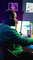 Vertical Audio composer playing piano electronic keyboard to create a new track, adjusting volume levels on old recordings. Music producer recording sounds, plays tunes on midi controller. Camera B. video