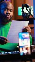 Vertical Talented composer explaining musical sheet notes during online master class recorded with smartphone in home studio. Artist musician teaching people how to read and sing accords on piano. Camera A. video