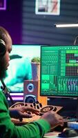 Vertical African american music producer twisting knobs on mixing console, produce tracks with sound effects. Artist composing songs in post production, operates on digital software in home studio. Camera A. video