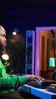Vertical Creative songwriter recording new tracks with microphone and midi controller, playing piano notes in home studio. Skilled musician composing music with electronic keyboard and stereo gear. Camera B. video
