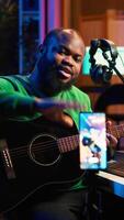 Vertical Professional composer teaching guitar lessons online on master class, recording himself playing acoustic instrument accords and explaining notes for tutorial. Young musician making vlogs. Camera A. video
