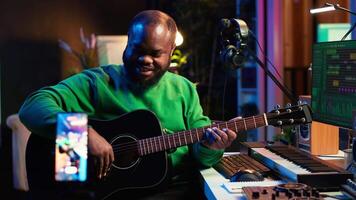 Guitarist instructor hosting guitar lessons online using a mobile phone, recording tutorial for master class. Artist musician explains acoustic instrument accords, assistance for beginners. Camera A. video