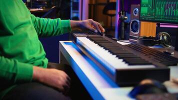 Music engineer producing song by mixing and mastering tunes on audio console, playing piano notes on synthesizer to record sounds on pc. Producer creating soundtracks with midi controller. Camera B. video