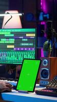 Vertical Young musician mixing and mastering songs next to isolated mockup display, operating on digital audio software to add sound effects on new tracks recorded. Audio engineer in home studio. Camera A. video