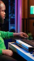 Vertical Sound engineer recording piano notes with DAW software in his home studio, working at night on producing new music with electronic tools. Musician composing tunes on midi controller. Camera A. video