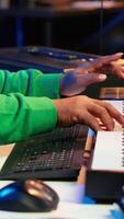 Vertical African american audio technician using piano synthesizer keys to add sound effects in post production, editing tunes with digital software and mixing console. Male artist in home studio. Camera A. video