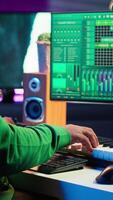 Vertical Musician playing piano keys and editing to improve sound quality of audio recordings in his home studio, putting on headset. Music producer uses midi controller to manipulate sounds. Camera A. video