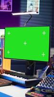 Vertical Musician operates on midi controller piano keys next to mockup screen, producing new songs with musical instruments and audio gear in home studio. Artist works with green screen. Camera B. video