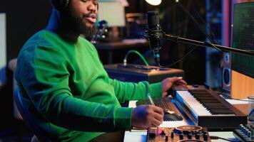 Professional artist writes new verses for a song in home studio, producing new music with mixing console and pc software. Composer works with audio equipment and tools, recording tunes. Camera A. video