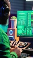 Vertical Young musician twisting knobs and mixing tunes with a console, following record settings on a digital software interface. Artist composer producing new music hits in his home studio. Camera A. video