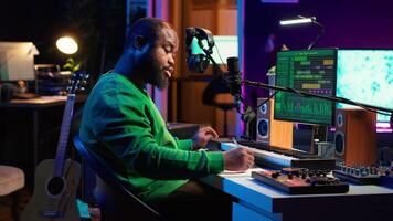 Songwriter taking notes to create new tracks for an album in his home studio, writing lyrics and harmonic elements before recording his song and editing on software, acoustical engineering. Camera A. video