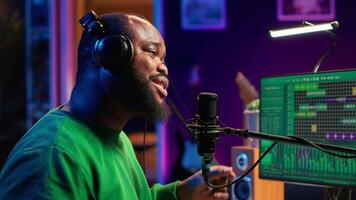 Confident artist singer performing a song on microphone in home studio, recording his audio files and manipulating raw sound on professional editing software. Music production. Camera A. video