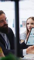Vertical Financial advisor showing statistical graphs on tablet to clients, analyzing market trends to optimize their income. Mother and daughter checking investment plan on device, camera A video