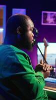 Vertical African american sound engineer using midi controller notes to add audio effects in post production, editing tracks with digital software and mixing console. Male musician in home studio. Camera B. video