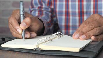 man hand writing on notepad while sited video