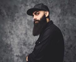 Muslim Man in Black Attire With Big Beard Against Gray Background photo