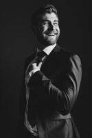Smiling Male Executive in Suit Adjusting Tie Against Dark Background photo