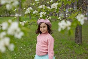 beautiful little girl stands under the branches of a blossoming white apple tree in the park. photo