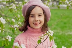 Portrait of happy little girl stands in a blooming white apple tree in the park. photo