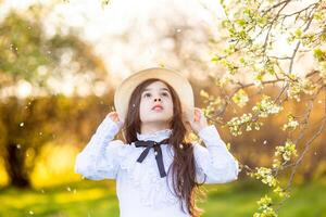 Beautiful girl in a white dress and hat, standing under flowering trees, in spring photo