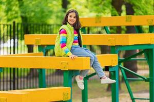 a cute smiling little girl, in a multi-colored striped jumper and a green vest photo