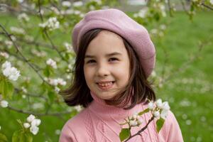 Portrait of beautiful happy little girl stands in a blooming white apple tree in the park. photo