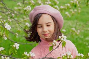 A happy little girl stands with her eyes closed in a blooming white apple tree in the park. photo