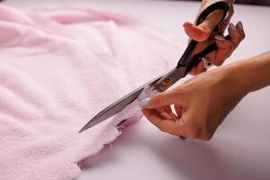 A man cuts pink fabric on a table with scissors. photo