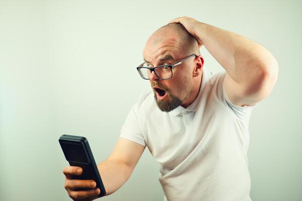 Portrait of surprised handsome bearded man with glasses and white shirt looking at mobile phone, facial expression, isolated on white background