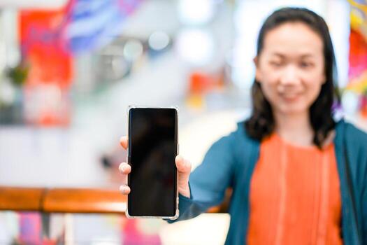 Black screen of mobile in Asian woman hand with blur face in department store background. For mock up website or application on smart phone. Clipping Path. photo