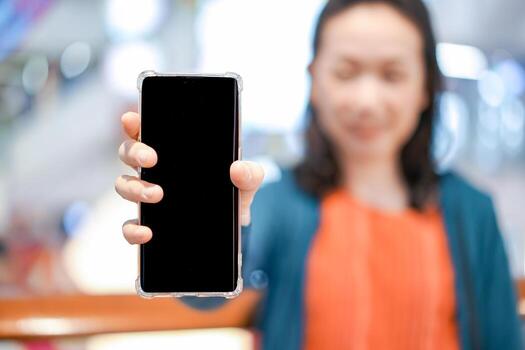 Black screen of mobile in Asian woman hand with blur face in department store background. For mock up website or application on smart phone. Clipping Path. photo