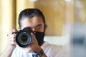 A man wearing black mask is shooting photo through a viewfinder camera with the right eye.