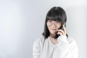 Isolated Pretty Asian glasses woman talks and speaks in the line with her mobile phone on white background in studio light. photo