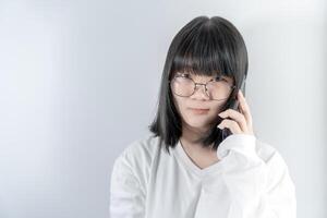 Isolated Pretty Asian glasses woman talks and speaks in the line with her mobile phone on white background in studio light. photo