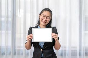 White Screen on Tablet was hold by the Asian eyeglasses woman, is smiling in front of transparent curtain. for mockup to present website or application on tablet computer. photo