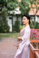 A woman in a traditional Thai costumes is standing on the wooden bridge while being taken a portrait photo shooting.