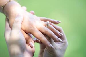 A man is wearing a wedding ring to a woman on his left ring finger. Close up on the hand in the outdoor field with the sunlight and tree shadow shading. photo