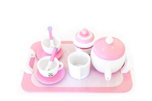 A set of pink white pastel color wood toy tea cups including 2 coffee cups with teaspoons, a teapot, a sugar jar and a milk jug is placed on a tray. Isolate clear on white background. photo