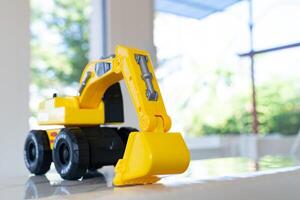 Backhoe loader, yellow construction toy vehicle with articulated parts built with sturdy plastic is placed on a table. photo