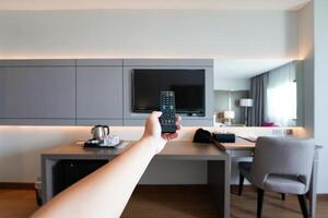 Watching TV using dust remote controller in the man's hand with resort hotel room blur the background at Nakhon Phanom Province, Thailand. photo