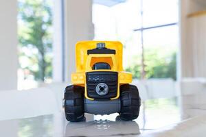 Dump truck, yellow construction toy vehicle with articulated parts built with sturdy plastic is placed on a table. photo
