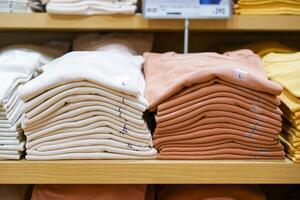 A pile of shirts, earth tone color, cream and brown was folded and put on shelf in cloth shop department store. photo