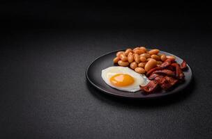 English breakfast with fried eggs, bacon, beans, tomatoes, spices and herbs photo