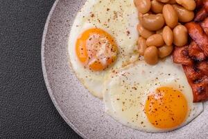 English breakfast with fried eggs, bacon, beans, tomatoes, spices and herbs photo