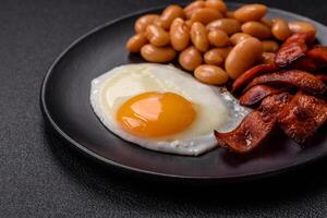 English breakfast with fried eggs, bacon, beans, tomatoes, spices and herbs photo