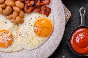 English breakfast with fried eggs, bacon, beans, tomatoes, spices and herbs photo