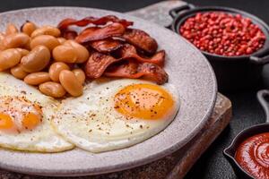 English breakfast with fried eggs, bacon, beans, tomatoes, spices and herbs photo