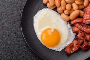 English breakfast with fried eggs, bacon, beans, tomatoes, spices and herbs photo