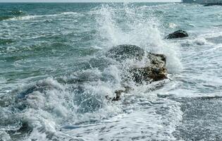 Sea waves crashing against rocks on a sand and stone beach photo